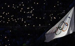 Smartphone lights illuminate the Olympic flag at the start of the closing ceremony [AP Photo/Natacha Pisarenko]